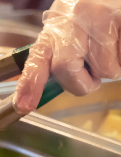Gloved hand of chef holding tongs and serving food at canteen counter