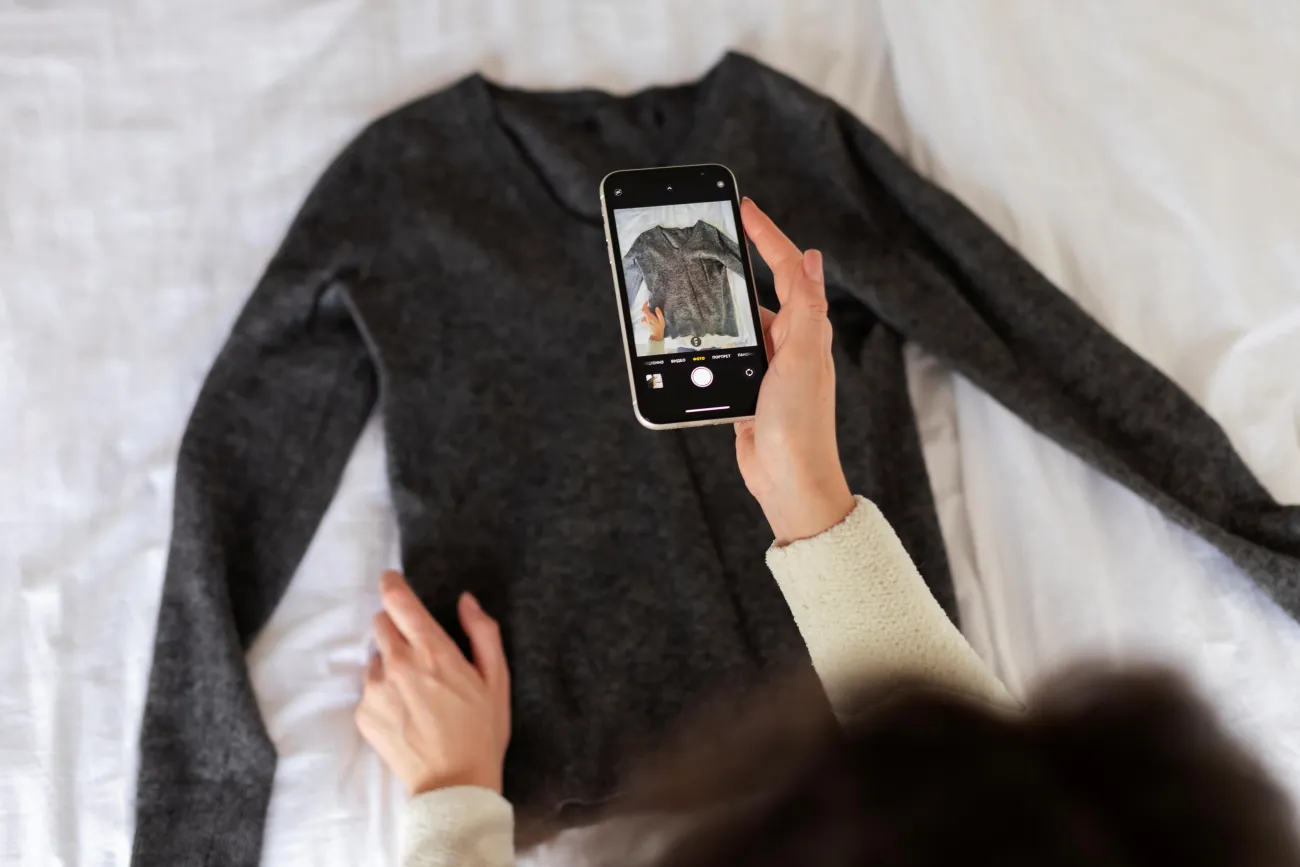 Hand holding a mobile phone while taking a photo of a jumper