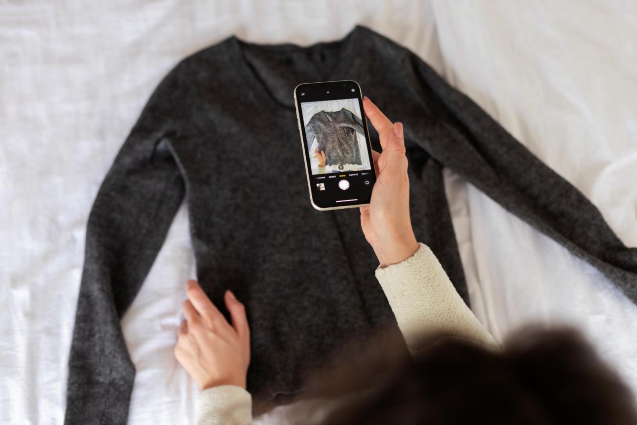 Hand holding a mobile phone while taking a photo of a jumper