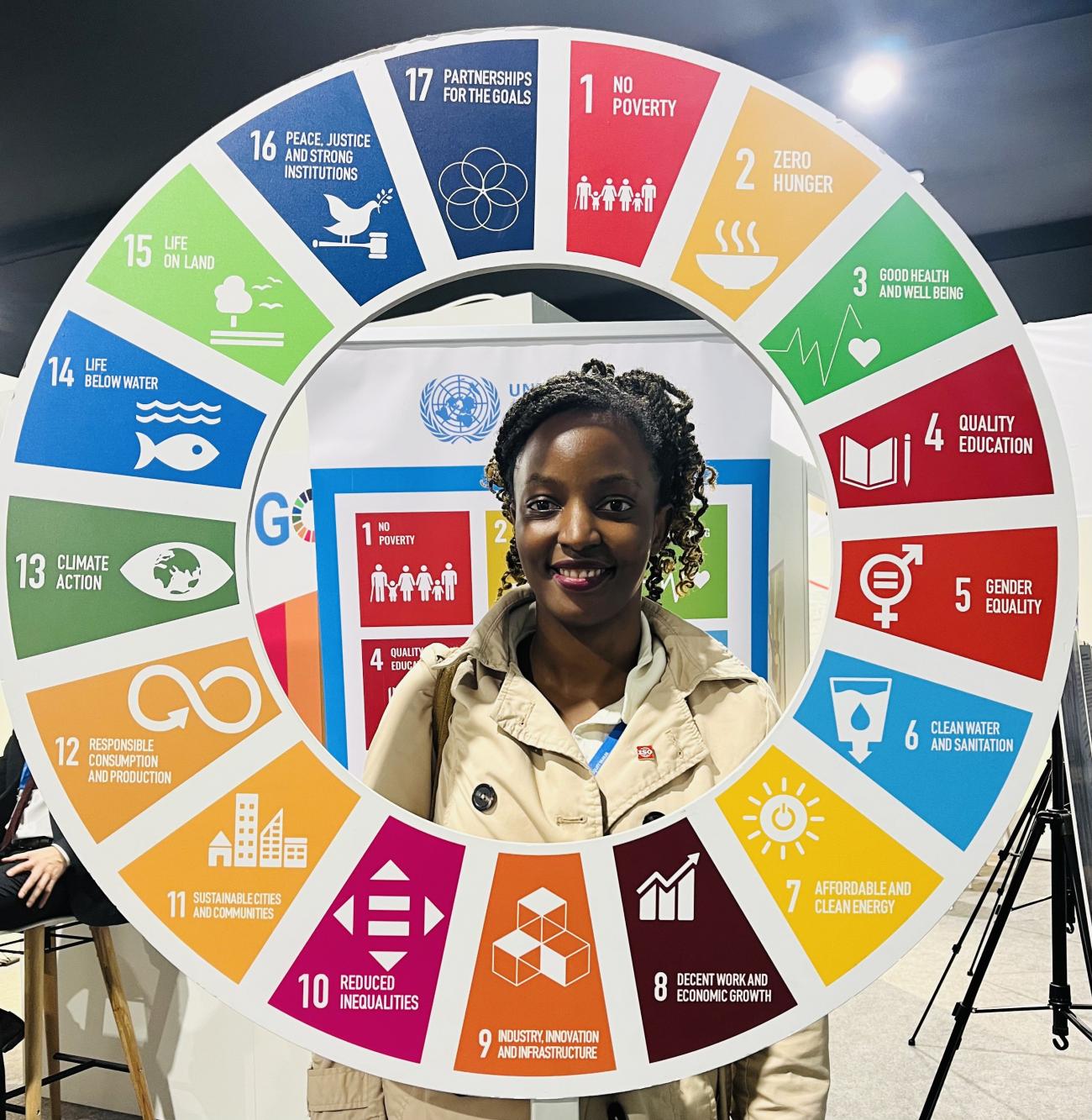 Rose Kobusinge with a circular sign showing the UN's Sustainable Development Goals (SDGs)