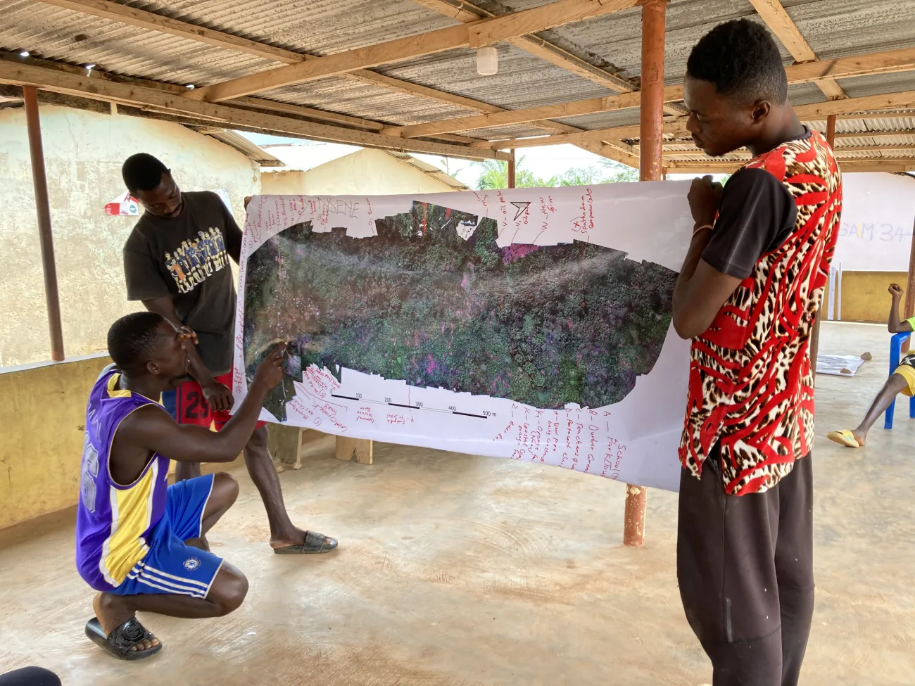 Three men holding a banner showing the mapping of their dronescape in Nsene, Central Region, Ghana