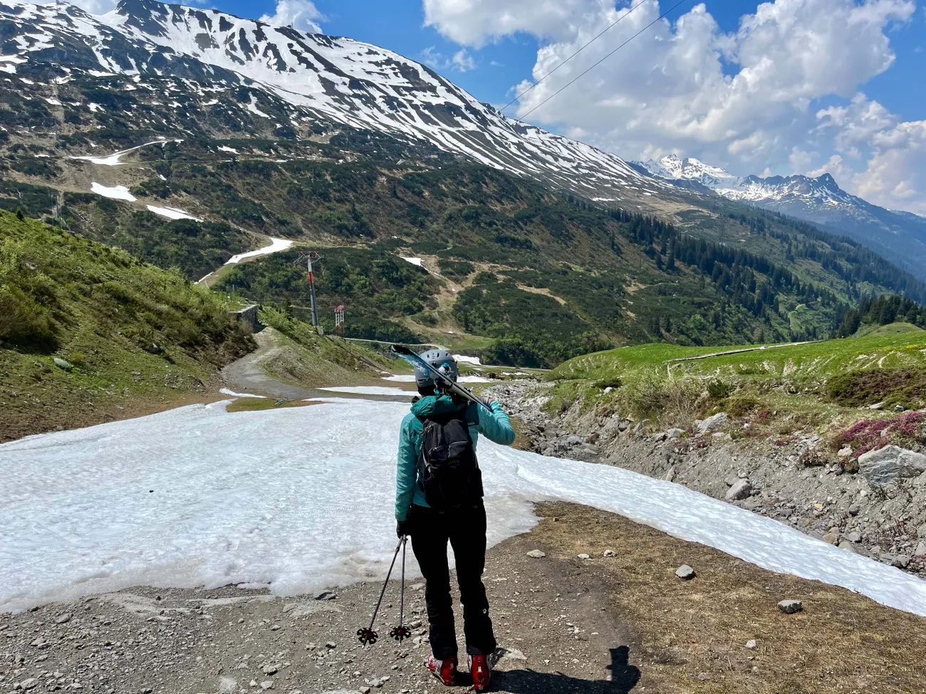 Skier carrying skis at top of slope with very little snow on it