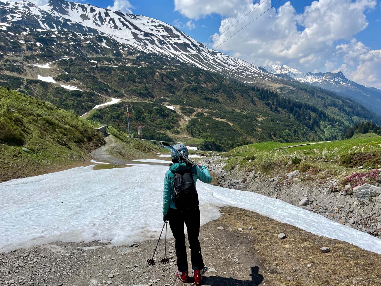 Skier carrying skis at top of slope with very little snow on it