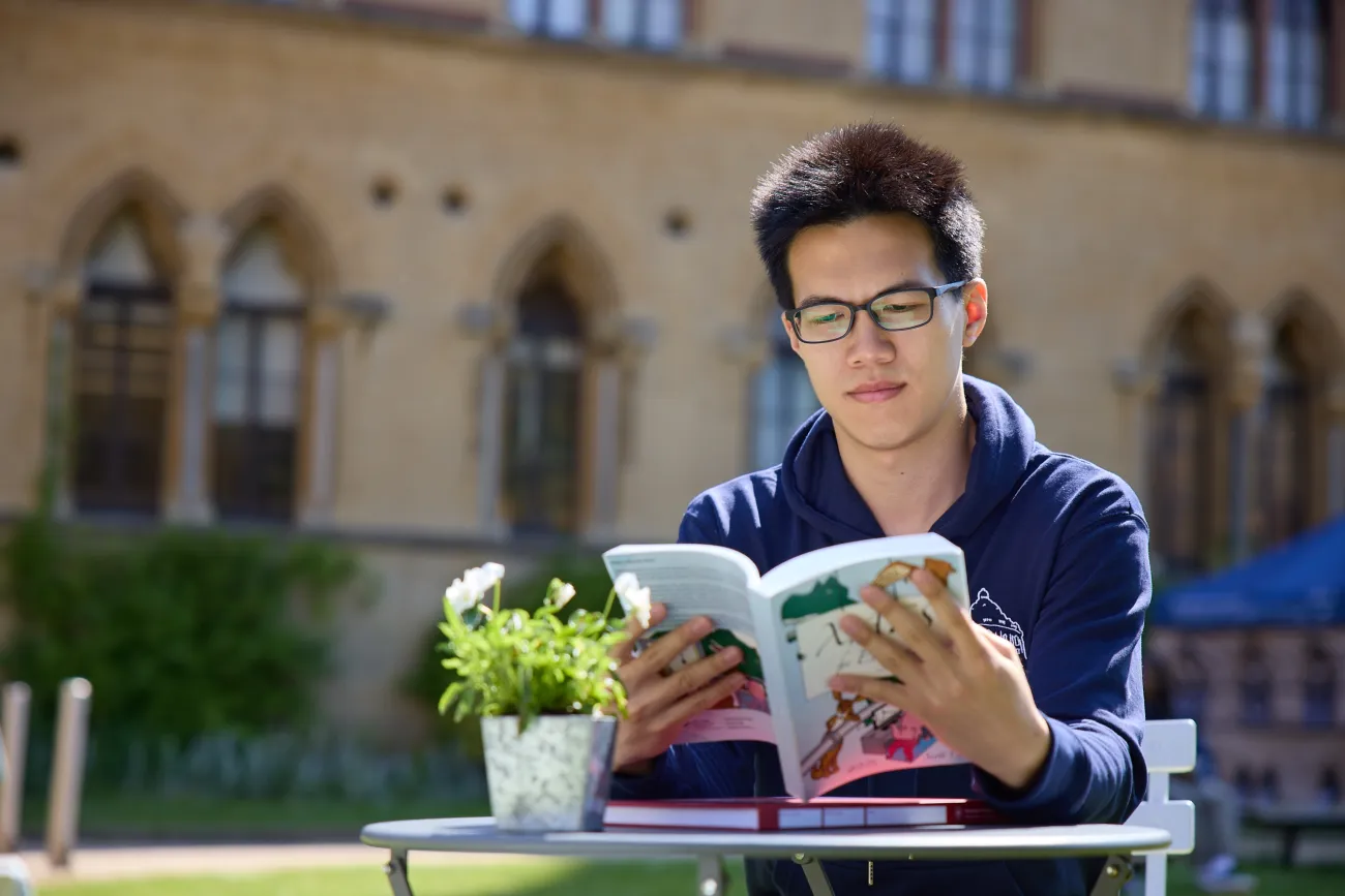 Student reading a book on grass outside an Oxford college