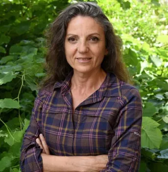 Professor Sandra Diaz in front of a leafy green bush