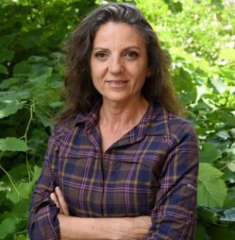 Professor Sandra Diaz in front of a leafy green bush