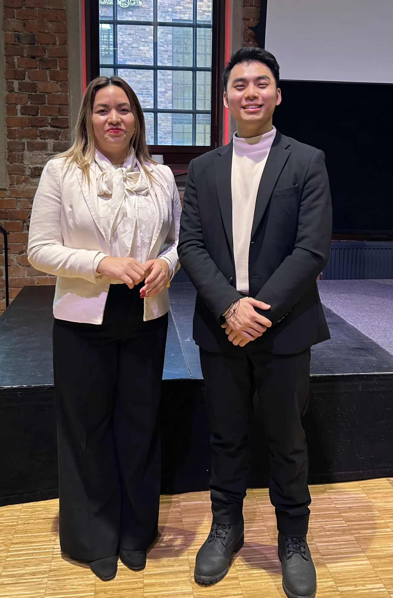 Max standing beside Patricia Godínez, the Ambassador of El Salvador to Sweden in front of a stage platform