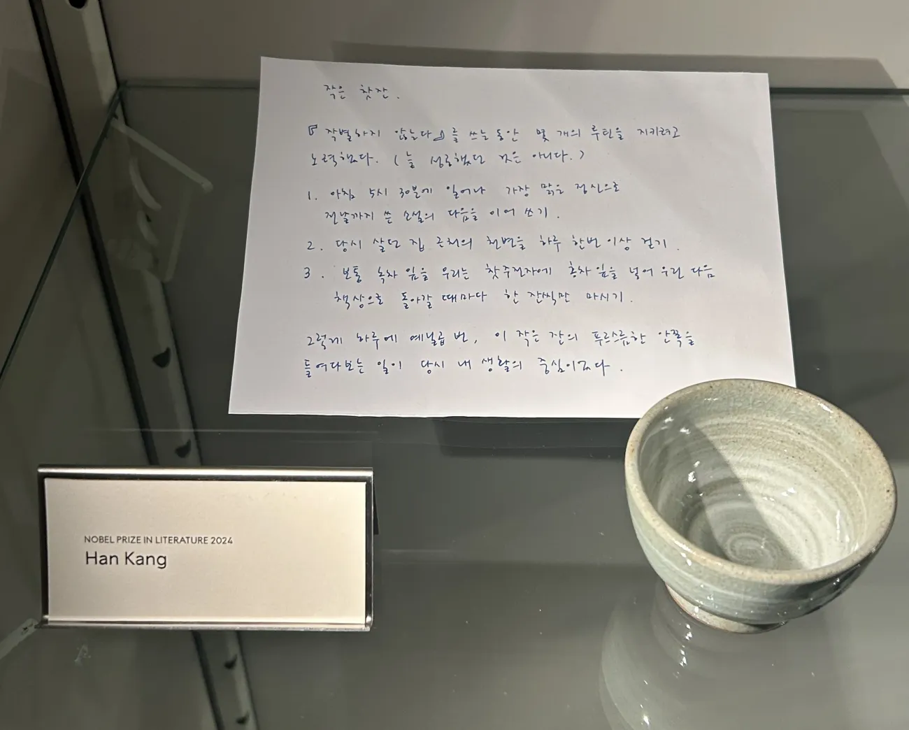 A handwritten note in Korean by Han Kang, 2024 Nobel Laureate in Literature, displayed alongside her personal cup with greenish blue circles
