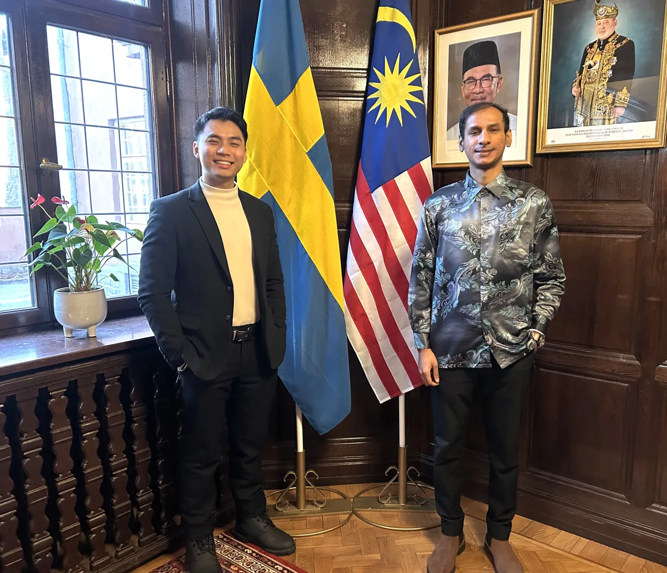 Max standing beside Theventhiran Arumugam, First Secretary, Embassy of Malaysia in Stockholm, Sweden, in front of the Swedish and Malaysian flags