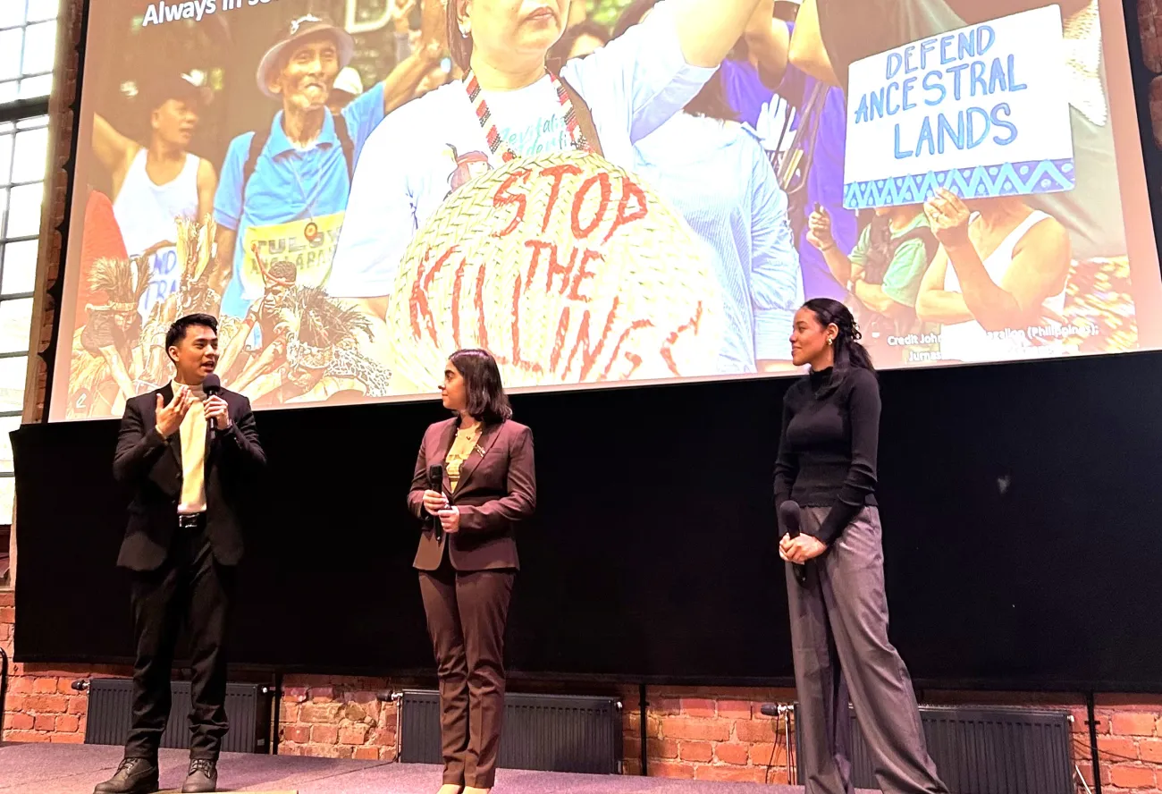 Max holding a microphone while speaking, alongside Melissa Okeke and Stefanie Karayoff presenting on environmental rights during Nobel Week