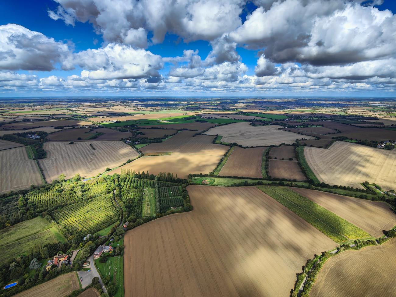 Aerial view of a typical British countryside patchwork. Agriculture fields, farm rural landscape, blue sky and white clouds.