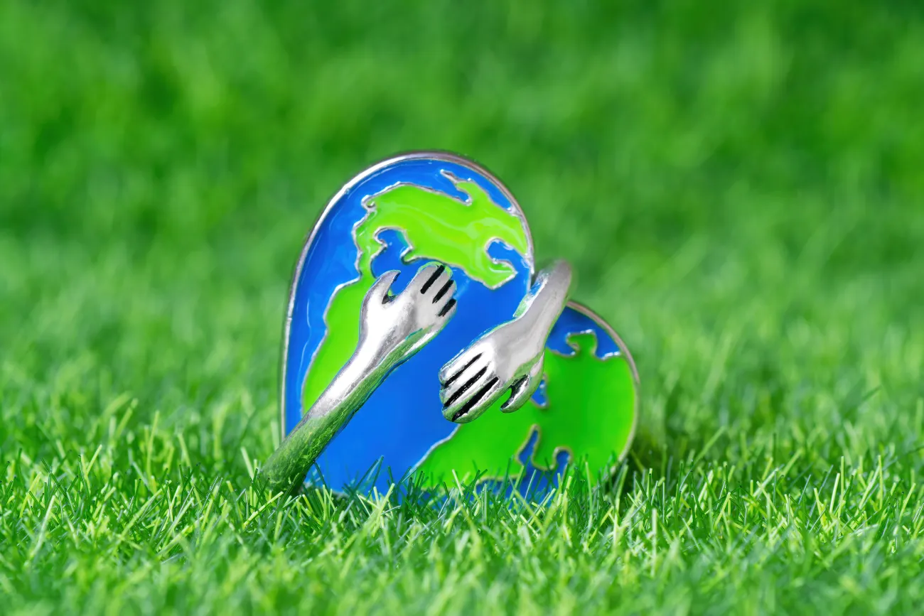 Close up of a metal pin badge of a heart shaped globe with small metal arms hugging it