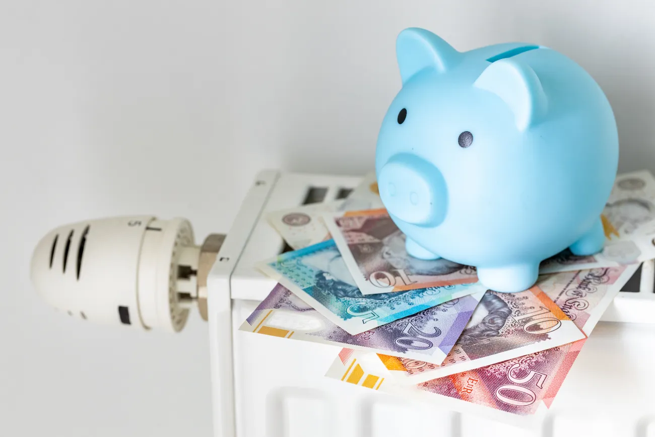 A blue piggy bank sat on British bank notes on top of a radiator