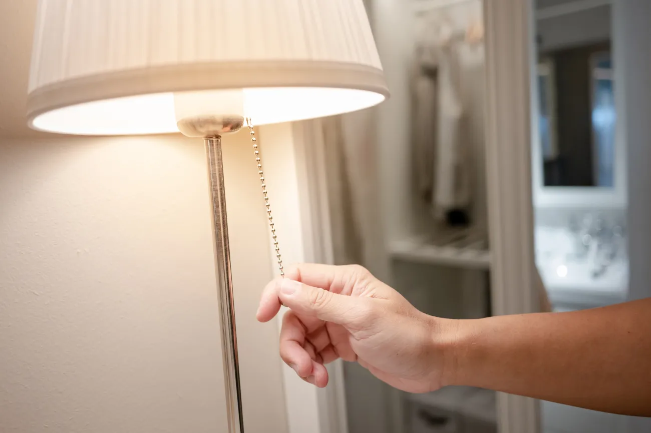 A hand turning off a table light with a pull cord