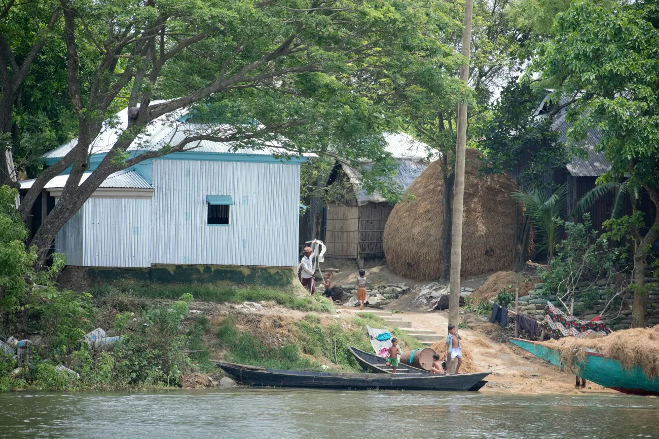 View of a homes on the riverbank at Kishoreganj, Bangladesh with children in a boat on the water