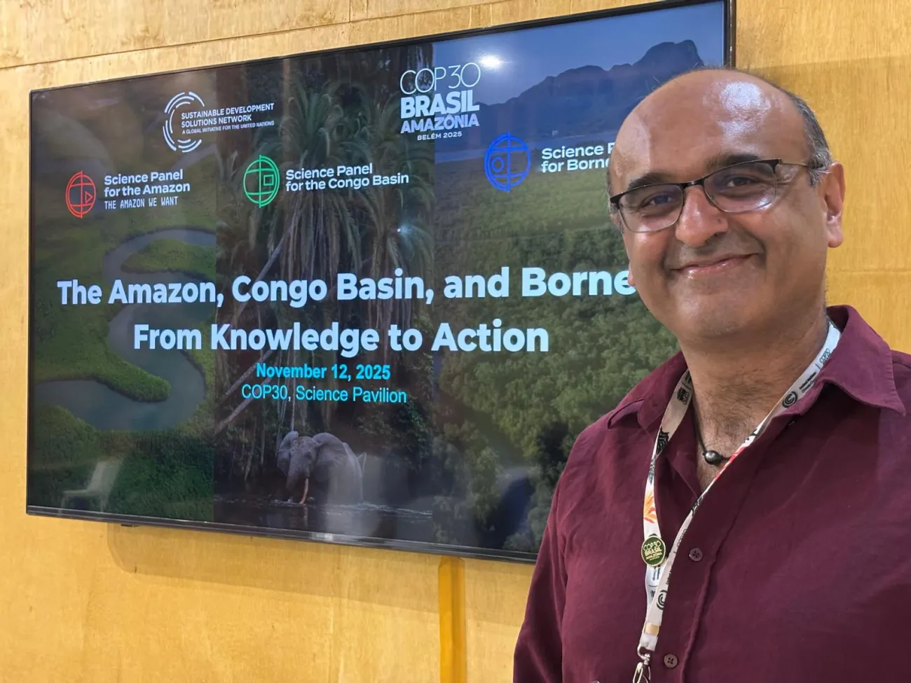 Prof Yadvinder Malhi standing next to the screen with the title of the event at COP30