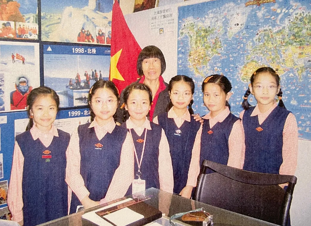 Natalie as a schoolgirl with classmates in pinafores in the classroom