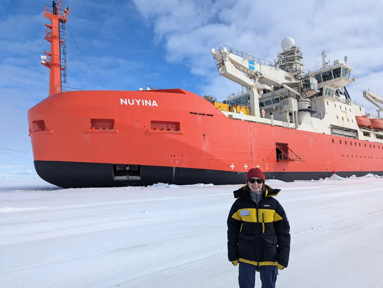 Samantha in her arctic clothing standing in front of the Nuyina at Davis Station