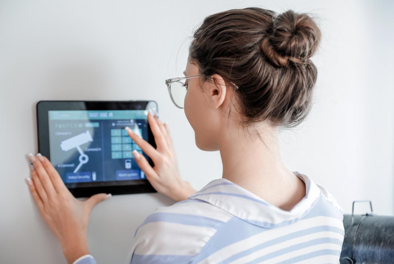 Woman facing wall of home and using smart home security system control panel