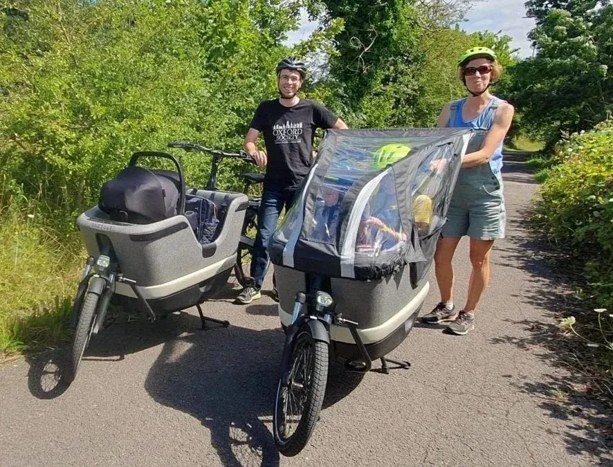 Two people standing holding bikes with large open basket shaped capacity in front one with small children