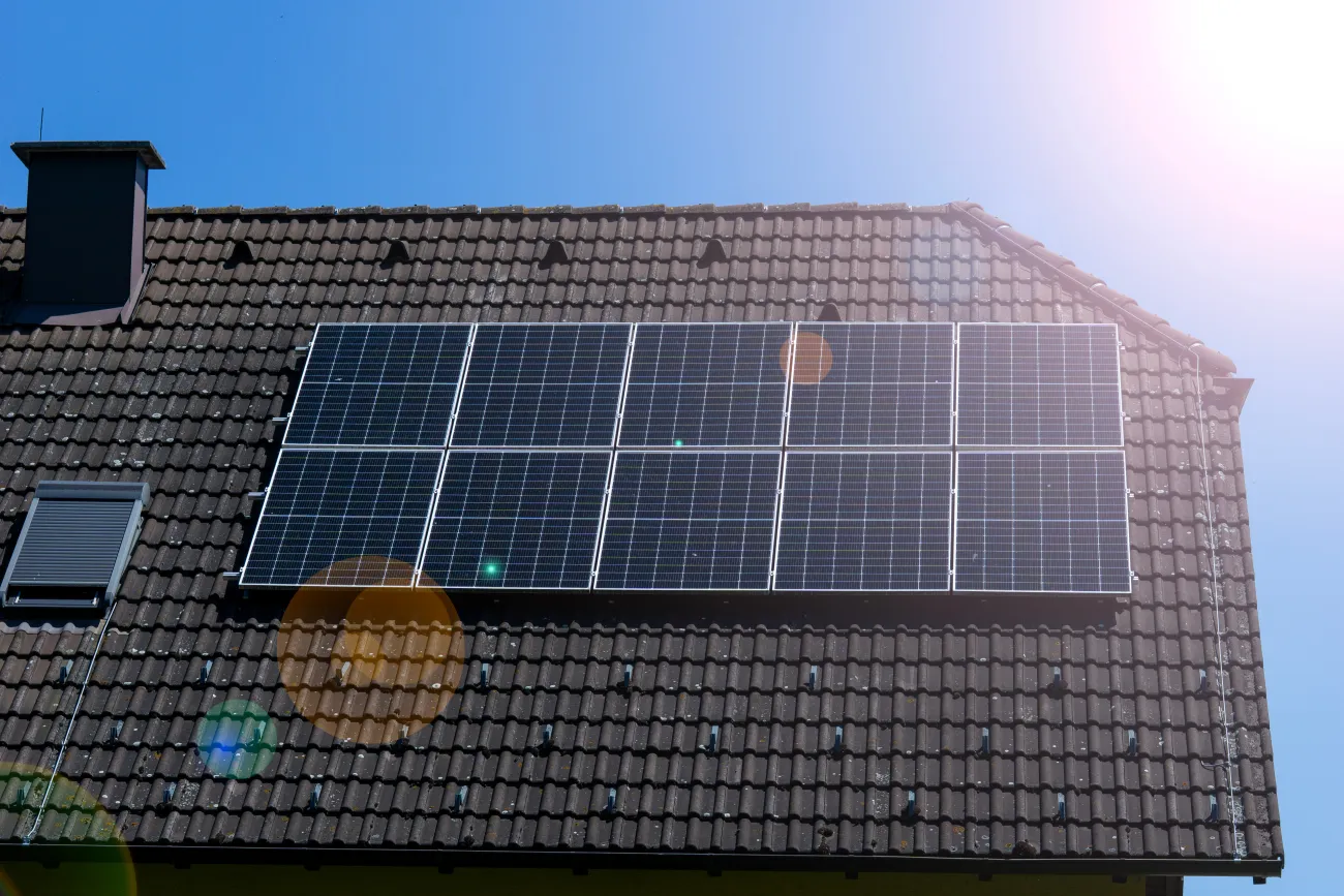 Solar panels on a tiles roof with a blue sky and the glare of the sun reflecting