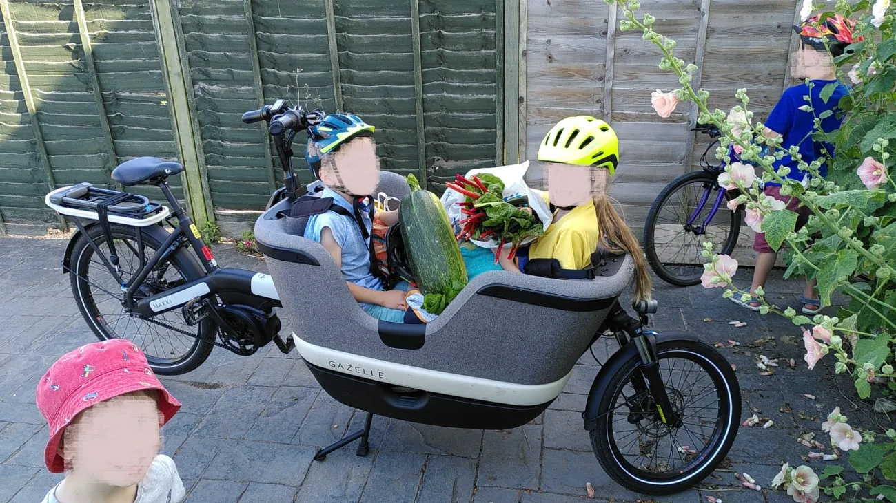 Stationary e-cargo bike with children sat inside holding items of shopping, with blurred faces