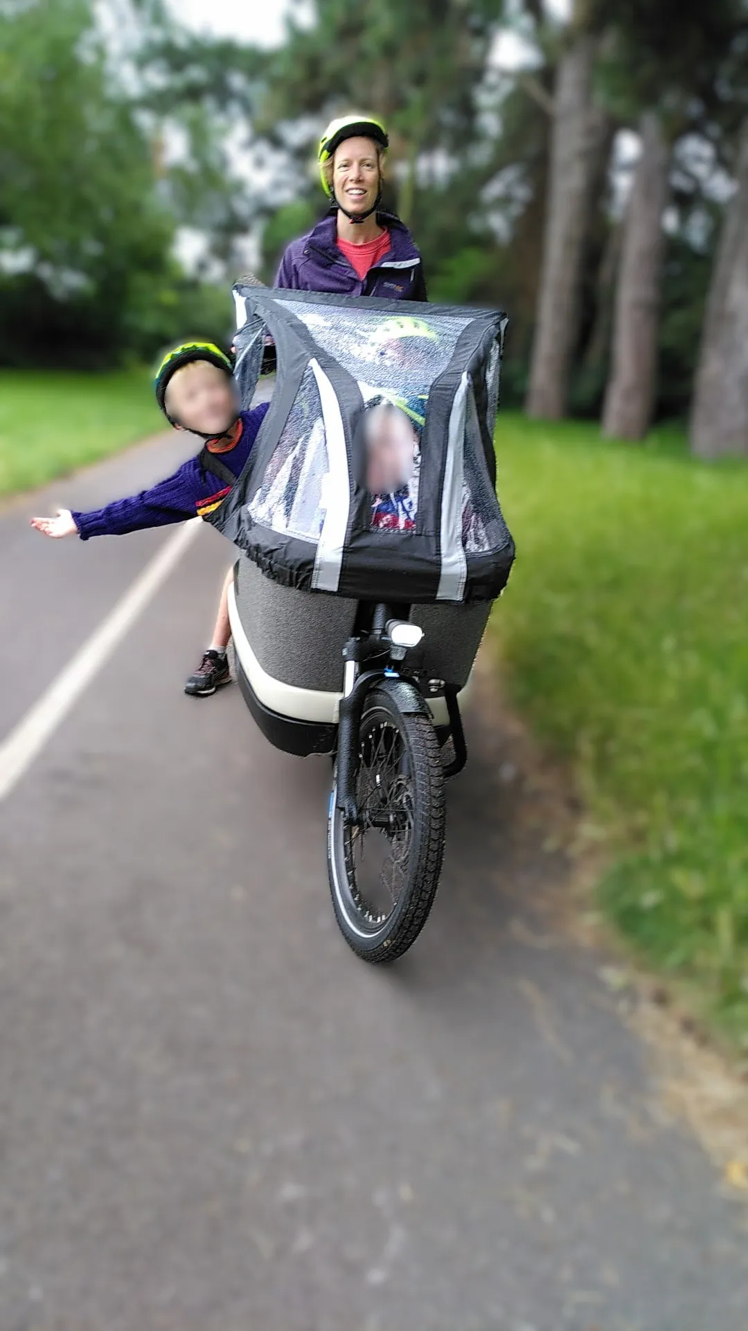 Mum riding e-cargo bike with child (blurred) leaning out and waving